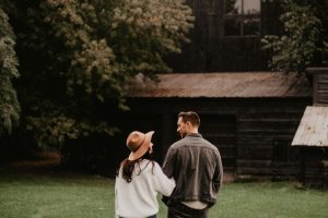 A couple walks through a grassy area towards a rustic barn, capturing a romantic autumn ambiance.